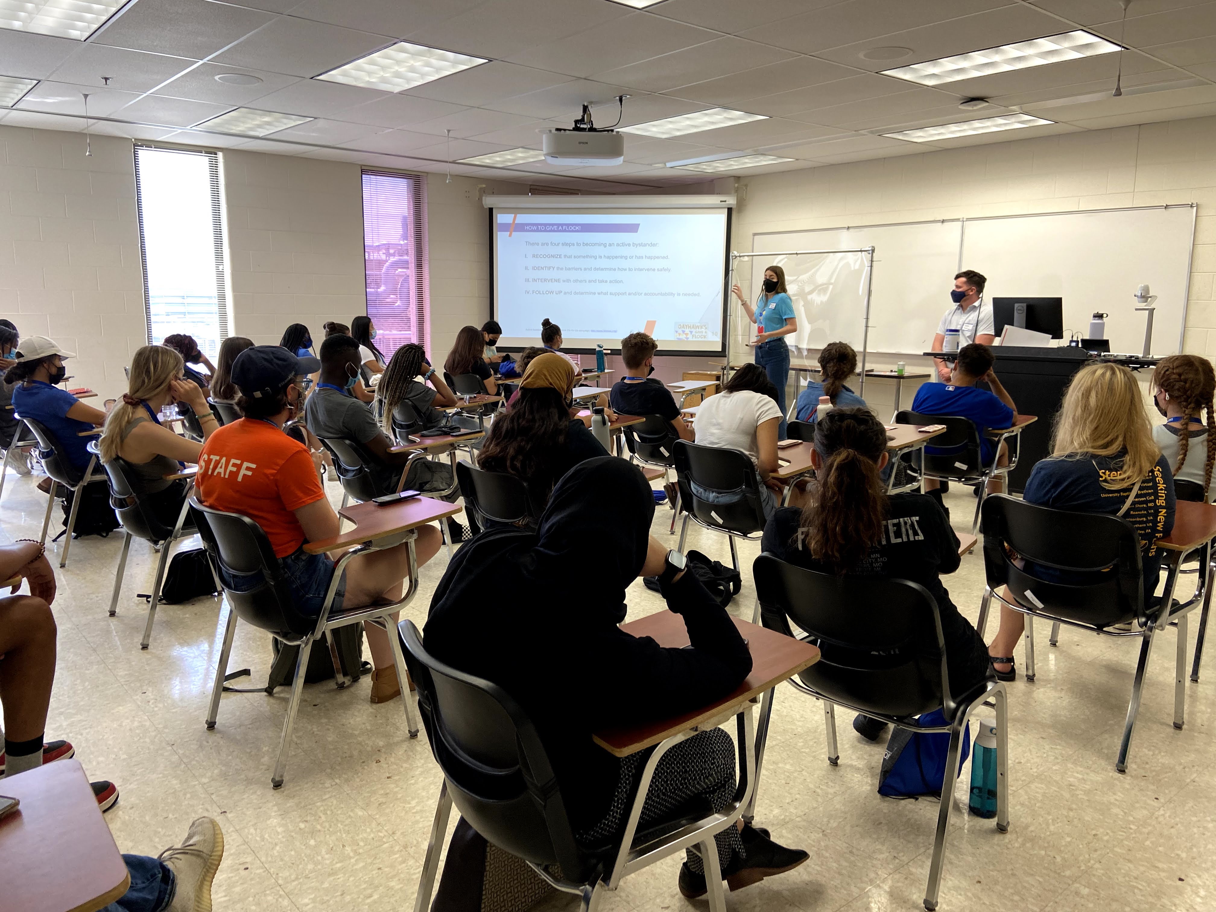 A group of students sitting in a classroom for Jayhawks Give a Flock. Two presenters are at the front of the room in front of a projector